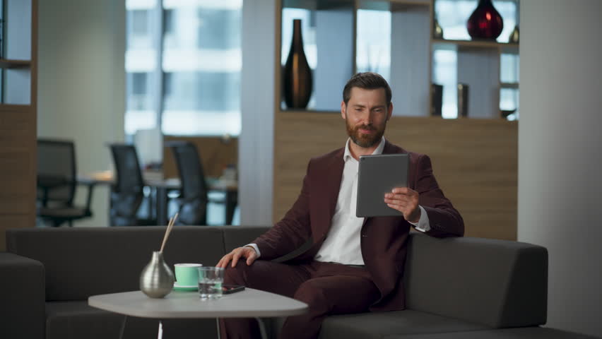 Smiling realtor man waving hand unknown people business video conference in big cabinet. Happy professional entrepreneur ending call deal at office interior. Modern digital successful work concept.