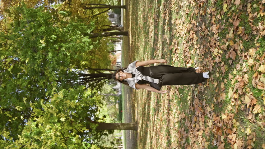 A smiling woman stands amidst autumn leaves in a sunny park, conveying a sense of happiness, youth, and natural beauty.