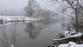 Beautiful cold winter landscape, snow near the river and trees with reflection in the water