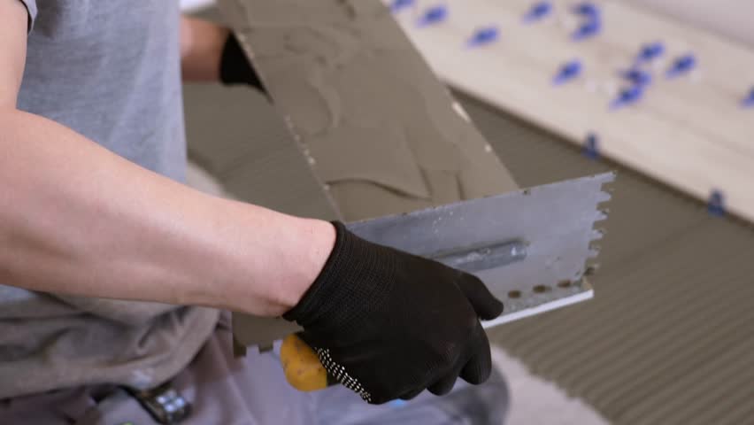 A tiler lays floor tiles on the floor. Porcelain tiles in the kitchen. A tiler is gluing tiles to the kitchen floor. A man is laying tiles on the bathroom floor.