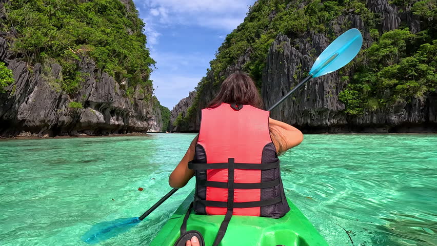 A kayaker navigates through the emerald waters flanked by towering tropical limestone cliffs, creating a sense of adventure. Slow Motion Camera 4K RAW.  Royalty-Free Stock Footage #3420591773