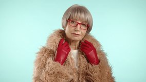 A poised woman in her 60s encapsulates winter chic in a fluffy tan faux fur coat, coordinating red gloves, and glasses, against a pastel blue background. Camera 8K RAW.