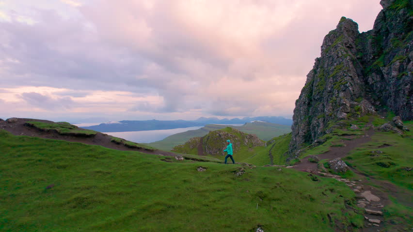 AERIAL: Tourist woman crossing the ridge towards impressive Old Man Of Storr. She hikes towards stunning rock formations at Trotternish Ridge on Isle of Skye. Breathtaking scenery at famous landmark.