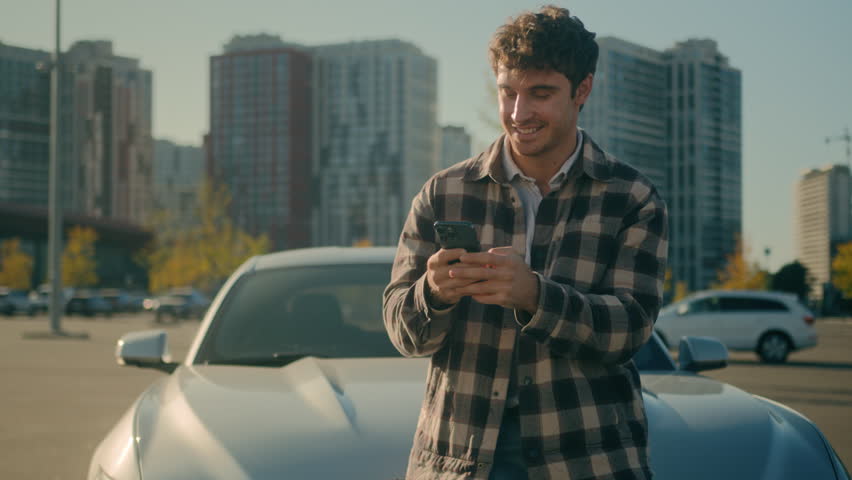 Caucasian successful man smiling client using smartphone outdoors happy male car driver businessman stand near new luxury auto in city surfing internet mobile phone application for electric automobile