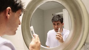 4k video footage clip young man brushing his teeth reflected in the mirror