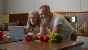 Older Caucasian couple middle-aged spouses family using laptop device at home kitchen choosing food delivery fresh vegetables online shopping natural products order retired woman and man laughing fun