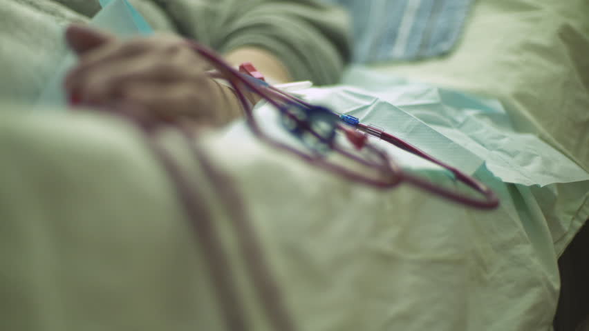 Focus change on the pipes injected in hand of hemodialysis patient during peritoneal dialysis treatment, dialyzer pumps blood that flows, shallow depth of field, macro shot, real scene, room interior