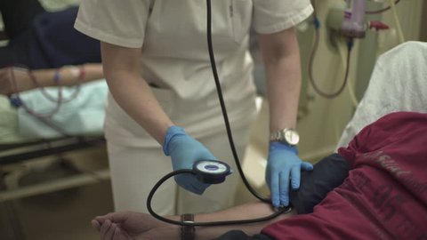 Caucasian charming nurse measures blood pressure of patient during hemodialysis treatment at hospital room, tilt up from male hand to portrait of woman, close up, shallow depth of field, real scene