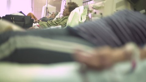 Mature female patients lying in the beds during hemodialysis treatment, focus change from portrait of elderly woman to hand during blood flows through the tube injected in vein, macro shot, real scene