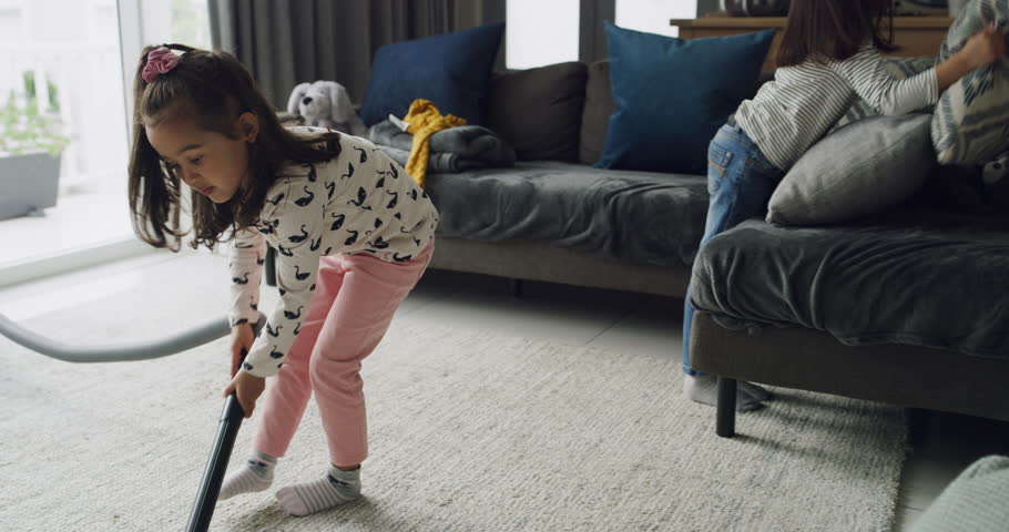 Girls, kids cleaning and vacuum carpet in living room, hygiene and housekeeping in home. Electrical appliance, children and housework on floor for chores of sisters together to help dust apartment