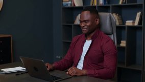 Medium shot of a young black man in profile in a shirt talking online with a client from home, online remote work, psychological session, online counseling, a man in shirt in the office at the table.
