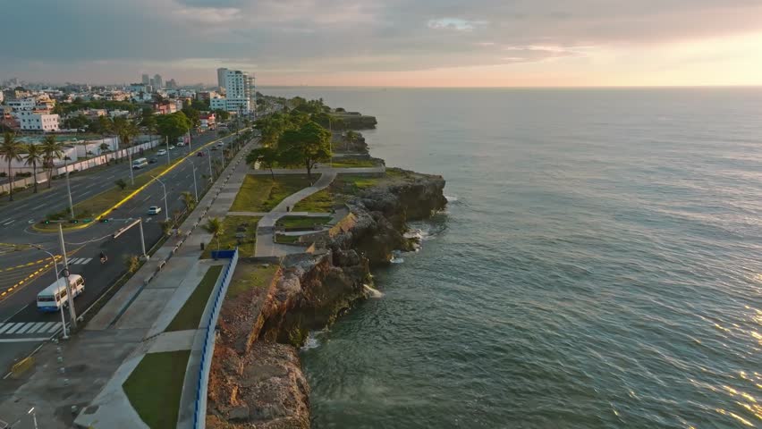 Aerial flight along coastline of Santo Domingo with traffic at MARITIMO PROMENADE during sunset time - Establishing drone shot Royalty-Free Stock Footage #3420882651