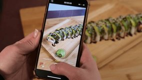 A young girl takes a vertical video of a prepared sushi dish on her phone. Records videos for social networks. Slow Motion