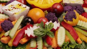 Sliced raw vegetables on a plate with hummus and white sauce. Vegetarian healthy food. A colorful arrangement for a buffet. Top view. Video looped