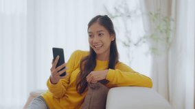 Happy young asian woman relax on comfortable couch at home texting messaging on smartphone, smiling girl use cellphone chatting, online shopping at home, video call communication