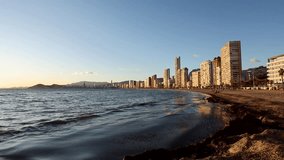 Slow motion video of sea and beach of Benidorm with skyscrapers in the background. Beautiful afternoon golden light