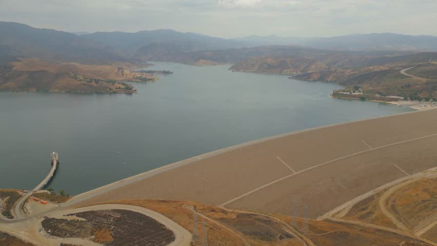 drone footage dam and reservoir in California ships float on the water stone shores mountains and hills covered with grass and trees