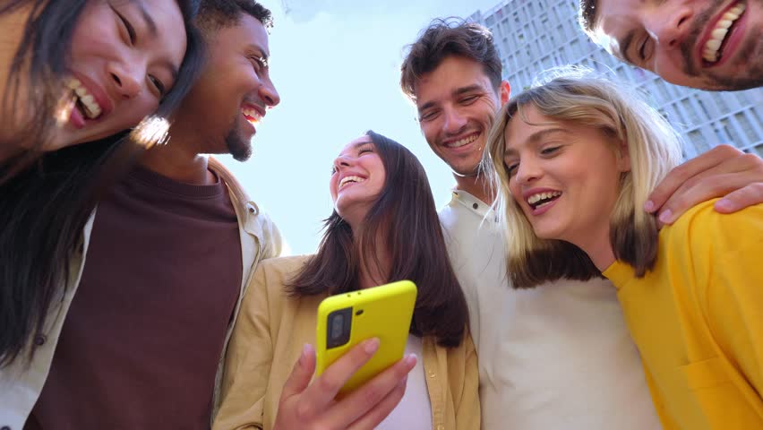 Happy group of people using having fun using smartphones at city street. Millennial generation friends laughing while watching social media content on mobile phone app. Technology concept