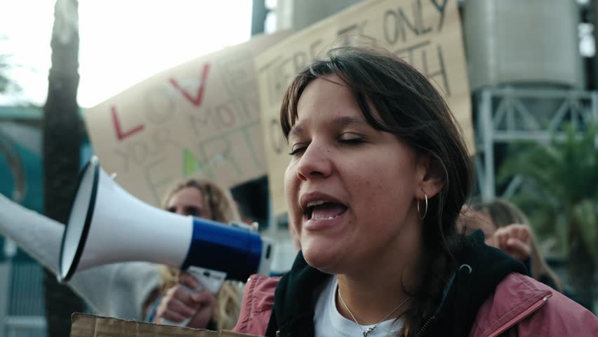 Close up Angry and rebellious woman speaking and protesting with megaphone at demonstration at climate change and global warming. Group of activists people at a pro-earth manifestation with banners Royalty-Free Stock Footage #3421214861