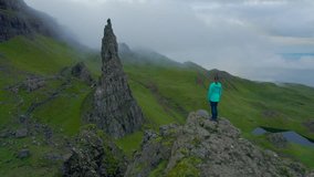 AERIAL: Woman admires breathtaking scenery while hiking to the Old Man Of Storr. Young tourist is impressed by unique landscape as she stands at viewpoint above Cathedral Rock on the Isle of Skye.