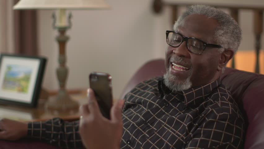 A happy elderly African American grandpa smiling and waving, chatting on a smartphone. Authentic family feel. Slow motion (48fps) Prores file. Royalty-Free Stock Footage #34212721