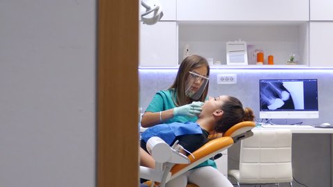 A moving shot in a dentists office, a young female dentist examining and working on the patients teeth, the shot is moving from left to right...