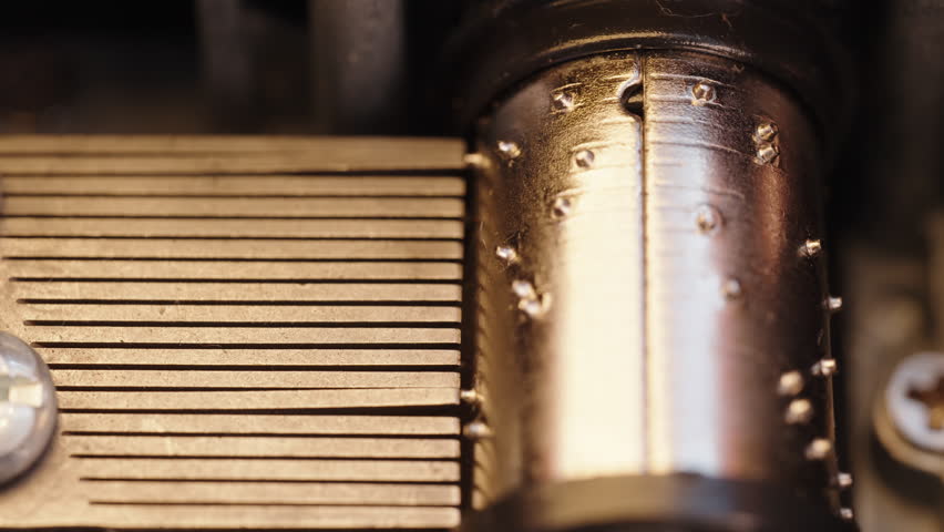 Detailed view of the interior of an old music box during play. Gears of the music box rotate. Flickering warm light from a flame.