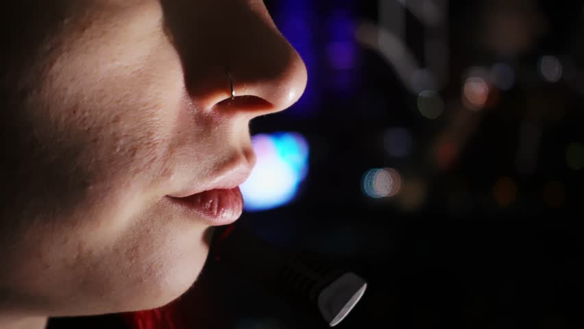 Closeup view of woman mouth taking by headset with a client sitting in the darkness on window background. Young adult caucasian lady is working in call center late at night and chatting with people