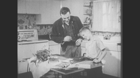 1950s: Boy stands up as man walks into kitchen and takes out a cigarette. Boy puts on hat and man hands him a lighter.