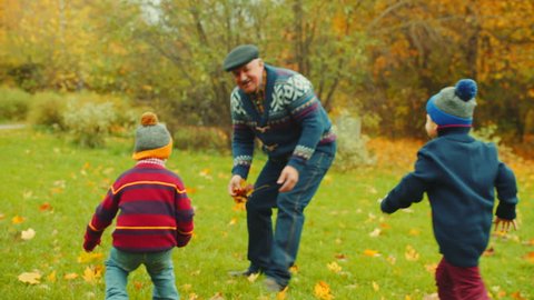 Grandfather is playing catch-up with his grandchildren in the autumn park