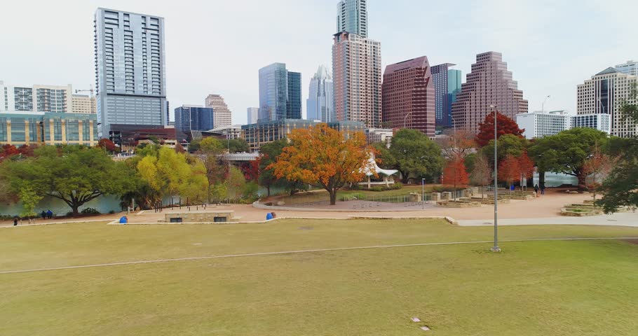 A dramatic rising aerial establishing shot of the Texas, Austin skyline with the Colorado River in the foreground. Late Autumn day with foliage trees.  	