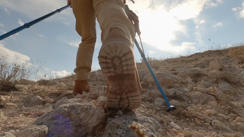 Two women friends climb to top of mountain in hiking boots with sun lens flares.