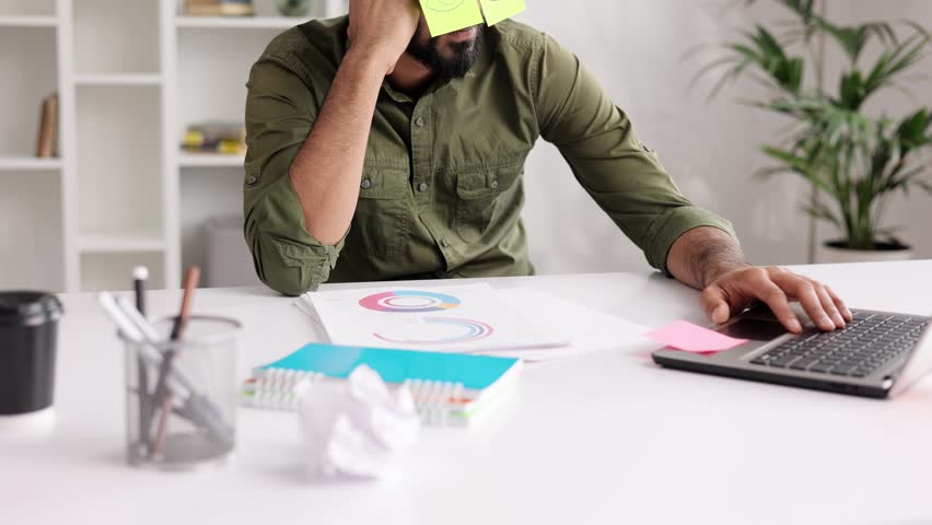 The concept of a lot of work. Tired Indian student boy sleeping with stickers on his eyes while sitting at the table. Distracted man in home office.