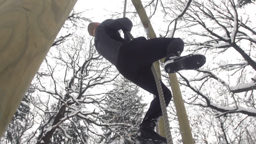 Slow Motion Of Young Sportsman Climbing Up The Rope Out In Snowy Nature