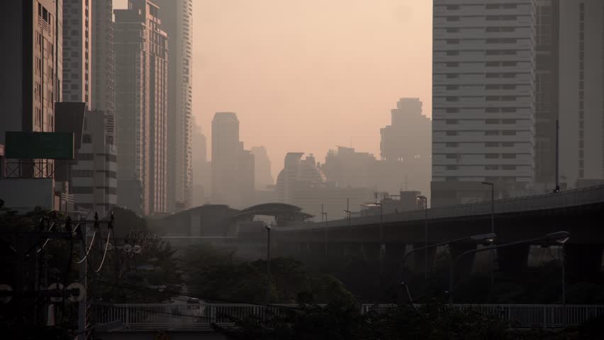 The cityscape of Bangkok is obscured by a thick blanket of dust and pollution . The heavy air pollution, filled with fine particulate matter (PM2.5), creates a hazy and oppressive atmosphere.  Royalty-Free Stock Footage #3421617771