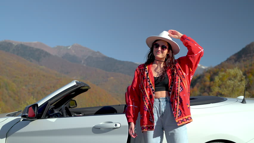 happiness and freedom in autumn vacation trip, carefree young girl taking off hat and enjoying life, portrait of woman in mountain landscape in sunny day, lady and white cabriolet