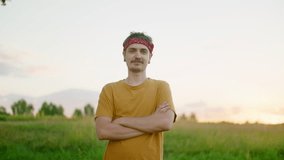Portrait of Young Caucasian hipster Man looking to camera and smiling outdoors with nature landscape. Mid hero shot of one confident fashionable guy with arms crossed. 4K orbit video with copy space