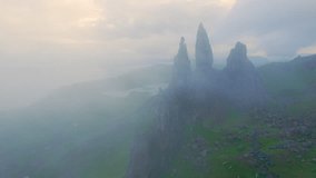 AERIAL: Mysterious Old Man Of Storr peeks through mist that shroud the mountain. Dramatic view of an iconic landmark on the edge of grassy Trotternish Ridge, famous natural attraction in Scotland.