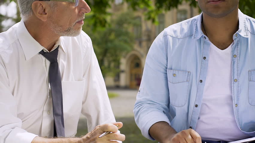 Student and professor communicating, sitting on bench in courtyard of university Royalty-Free Stock Footage #34217530