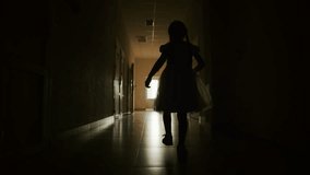 Girl child in dark empty corridor. Little girl looks out of window, rear view. Lonely silhouette of child running down dark corridor towards door and light. Primary school looking to future of child - Powered by Shutterstock - Get 15% off with code: PIKWIZARD15