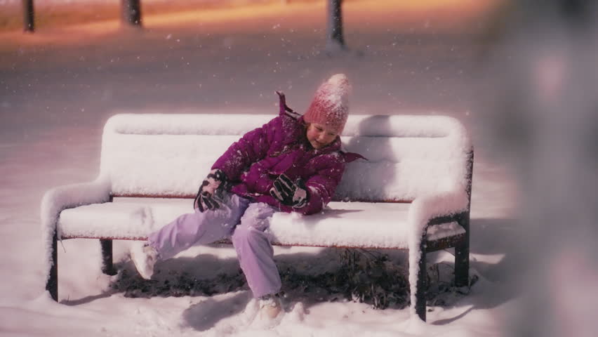 Little Caucasian Girl Lies on a Snow Covered Bench in the Park at Night