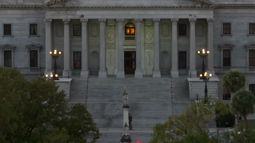 Tight aerial view of South Carolina State House. Drone rising shot with zoom lens during Columbia, SC sunrise. Williams Brice USC football stadium in background.