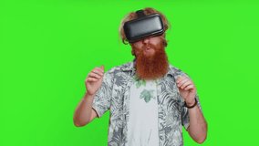 Excited happy bearded man using headset helmet app to play simulation game. Watching virtual reality 3D 360 video. Redhead guy in VR goggles isolated on green chroma key background. Future technology