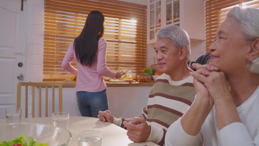 Asian lovely family having lunch, enjoy eating party in house together. Attractive senior elderly grandparent and young beautiful daughter eat foods celebrate weekend reunion at dining table at home.

