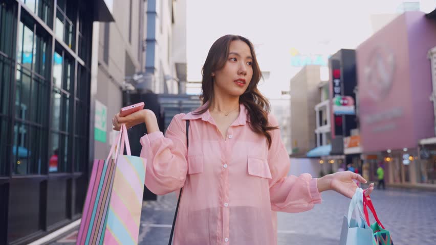 Asian young beautiful woman shopping goods outdoor in department store. Attractive female holding shopping bags then walking alone with happiness, enjoy purchasing in shopping mall marketplace center. Royalty-Free Stock Footage #3421886181
