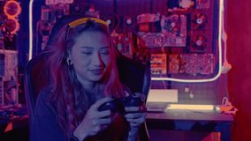 Young woman live stream she play video game at home neon lights living room, Gamer playing online game application on mobile smart phone wear gaming headphones, E-Sport concept