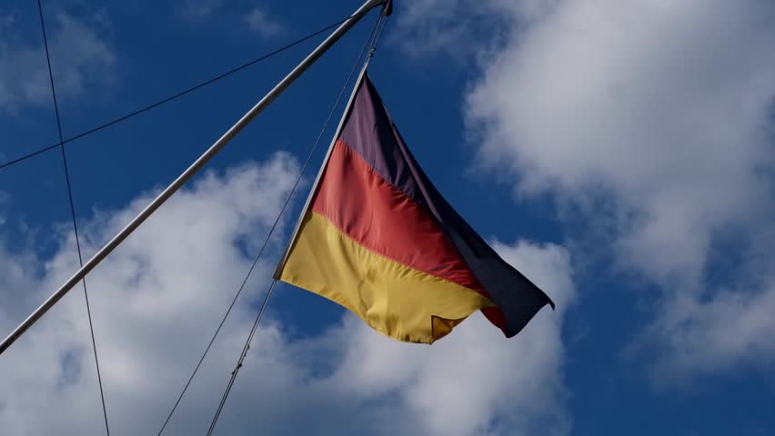Flag of Germany, waving on a blue sky background. Black red golden colored national banner, ensign, pennant, standard on a mast. Slow motion video