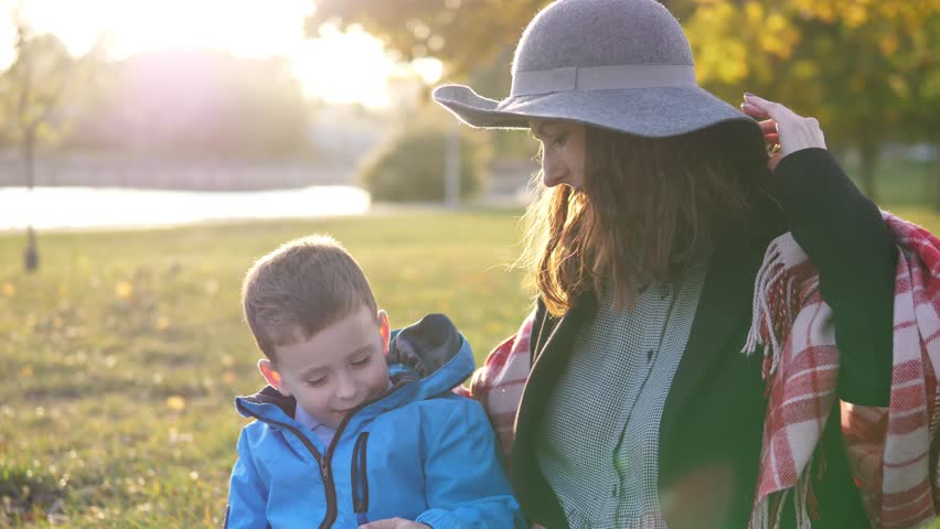 Mom and little son in the park on a picnic watching cartoons on a smartphone via the Internet