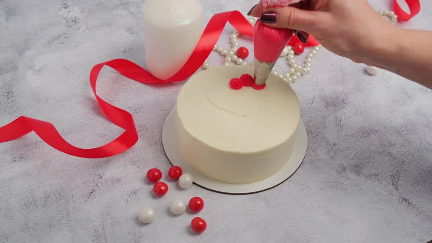 A pastry chef decorates a cake with red heart-shaped cream for Valentine