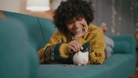 Young woman is throwing money in the money box. African american teenager putting coin in pink piggy bank at home. Girl saves money in moneybox, coin box. Saving money, self finance, capital concept. - Powered by Shutterstock - Get 15% off with code: PIKWIZARD15